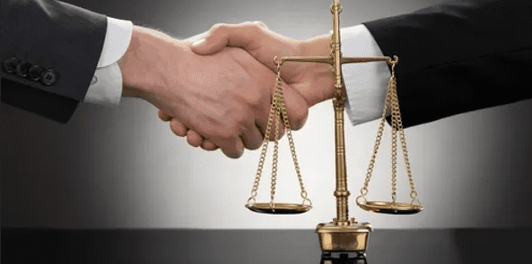 A handshake taking place behind the Scales of Justice